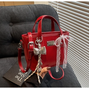 Detail of red glossy bucket bag with silver bow charm and white lace decoration
