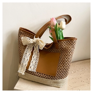 Détail du sac cabas en paille tressée avec poche en cuir brun et nœud en dentelle blanche