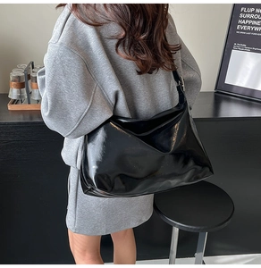Model wearing a large black patent leather tote bag over the shoulder in a modern room