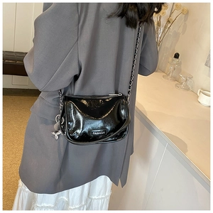 Close-up of elegant black glossy patent leather crossbody bag with chain strap and pendant
