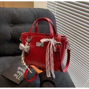 Detail view of red leather bucket bag with white lace bow and silver charm on sofa