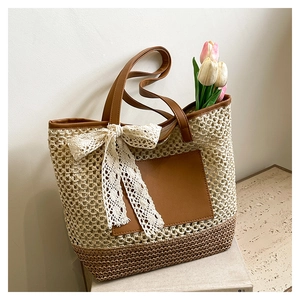 Détail du sac cabas en paille avec poche en cuir marron et nœud en dentelle sur pierre
