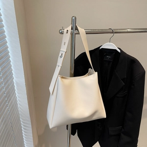 Detailed view of a white minimalist leather bucket bag with an adjustable metal buckle strap