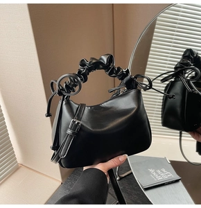 Detail of black pleated handle handbag with detachable strap on a mirror surface