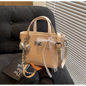 Detail of cream bucket bag featuring lace bow and silver butterfly charm decor