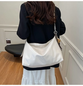 Detailed close-up of glossy white large hobo bag with metallic ring and woven charm