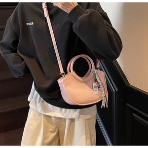 Detail of pink crescent bag showing polished texture, top handle, and beaded tassel
