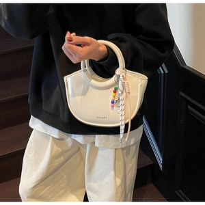 Close-up of white glossy crescent handbag with curved handle and beaded ornament