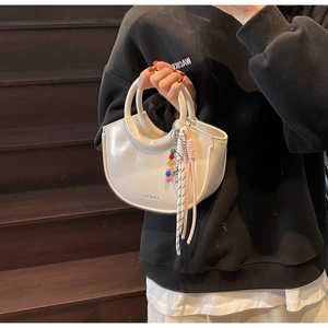Close-up of white glossy crescent bucket bag with colorful bead and ribbon charm
