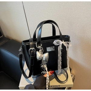 Detail of glossy black bucket bag featuring silver bow charms and white lace ribbon