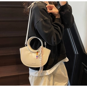 Detail of off-white crescent handbag with beaded charm on dark wooden stairs