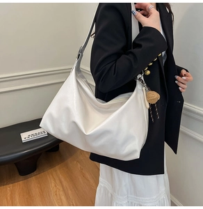 Detail of white glossy leather hobo bag featuring wide adjustable strap and bear charm