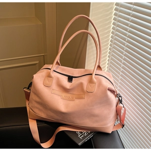 Détail d'un grand sac de voyage rose avec bandoulière réglable sur canapé noir