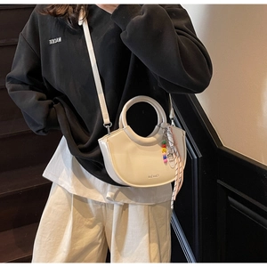 Detail of white semi-circular handbag with round handle and striped ribbon charm