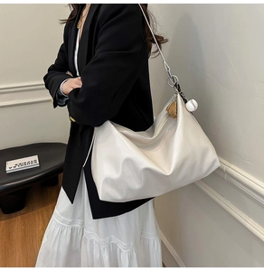 Detail of a large white hobo shoulder bag with glossy finish and baseball charm accessory