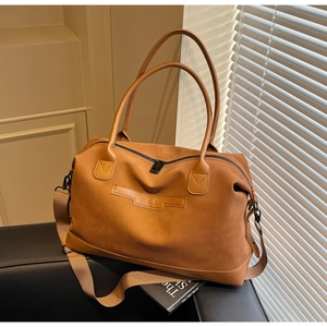 Détail d'un grand sac cabas marron caramel avec poignées sur un fauteuil en cuir noir