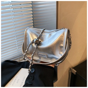 Detail of silver metallic handbag with chain strap and spherical charm on light background