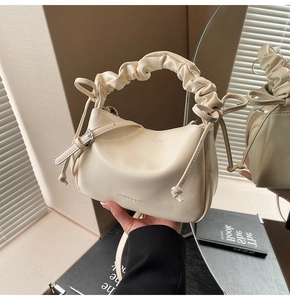 Close-up of cream white dumpling bag with bow ties and ruched handle texture