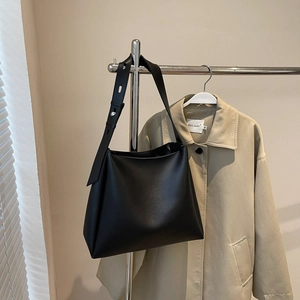 Detail view of a black minimalist bucket bag with adjustable wide shoulder strap and metal buckle