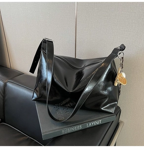 Close-up of black glossy leather tote bag with silver ring and shell charm detail