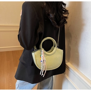 Detail shot of light green leather crescent bag featuring a circular handle and woven charm