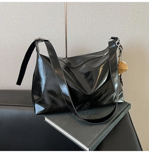 Detail of glossy black patent leather tote bag with a cute bear charm accessory