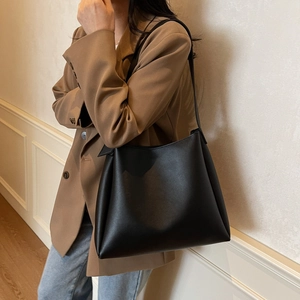 Side view of a minimalist large black leather bucket bag worn with a brown blazer