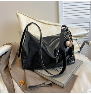 Close-up of black glossy hobo bag with unique baseball glove charm and leather strap