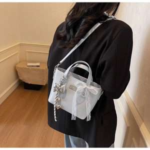 Light blue glossy bucket bag with lace bow and metal pendant on a black blazer