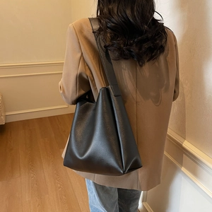 Close-up of a black matte leather tote bag worn by a model in an elegant professional style