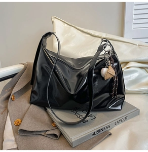 Macro detail of black glossy leather hobo bag with unique baseball charm accessory