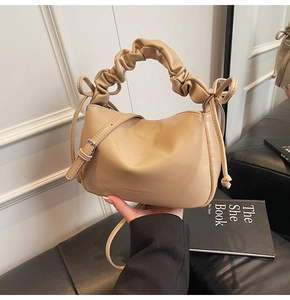 Detail of beige pleated handbag with bow accents and adjustable shoulder strap