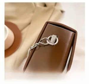 Detail shot of silver metal lobster clasp and ring on a dark brown leather bag