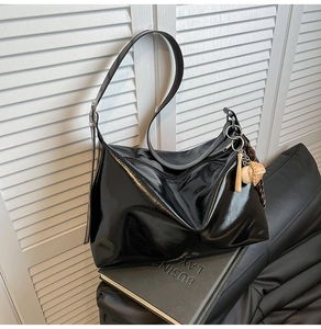 Detail of glossy black patent leather tote bag with silver buckle and baseball charm