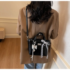 Detail of glossy black crossbody bag with silver bow charm and lace ribbon on a model