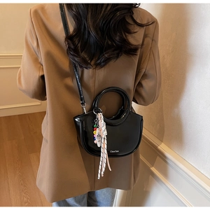 Detail of a black glossy handbag with circular handle and a colorful beaded tassel charm