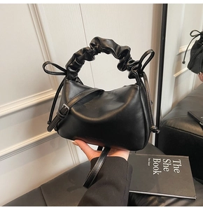 Close-up of black leather bag featuring a ruched cloud handle and bow drawstring detail