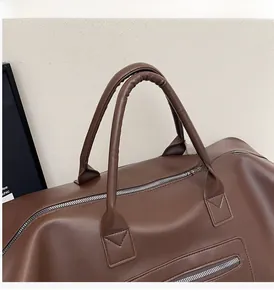 Détail des poignées rondes renforcées et du zip argenté sur le sac de voyage marron