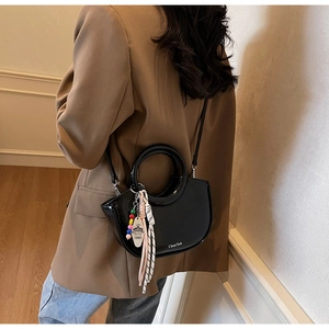 Detail of glossy black leather handbag with a crown charm and colorful beaded strap