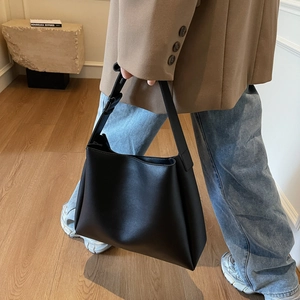 Macro view of black leather tote bag showing smooth matte texture and adjustable strap