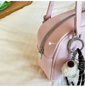 Detailed shot of pink faux leather bag featuring silver zipper and plush pompom charm
