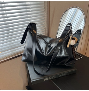 Detailed view of black patent leather tote with glossy finish and baseball charm