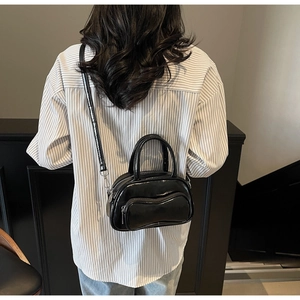 Gros plan du sac bandoulière noir brillant avec poche zippée à volants porté par le modèle