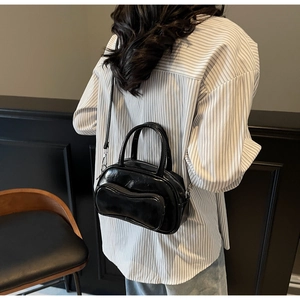Détail du sac Boston noir brillant avec une poche zippée élégante en forme de vague
