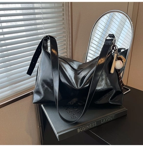 Detail of glossy black leather tote bag with a unique baseball pendant on a book
