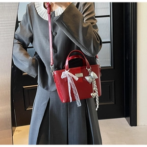 Detail of red patent leather bucket bag featuring white lace bow and silver pendant