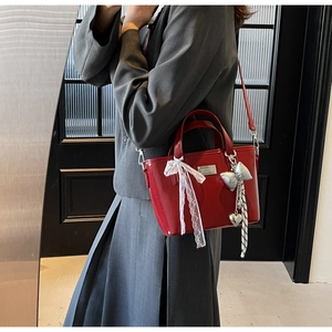Close-up of red patent leather bucket bag with white lace bow and silver charms
