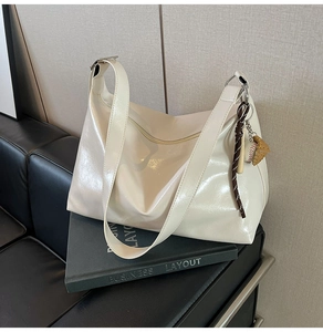 Close-up of glossy cream tote bag with baseball charm and wide strap on a book