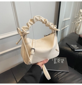 Close-up of cream shoulder bag featuring pleated handle and side ribbon bow details