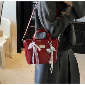 Detail of red glossy shoulder bag featuring lace bow and metallic butterfly charms